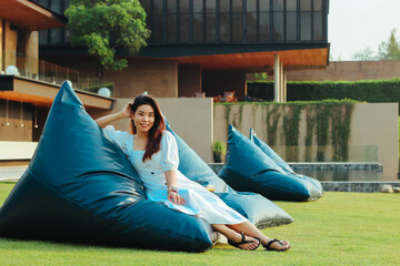 Beautiful Asian woman relaxing on blue bean bag chair on the grass near river