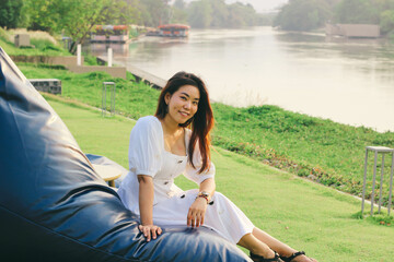 Beautiful Asian woman relaxing on blue bean bag chair on the grass near river