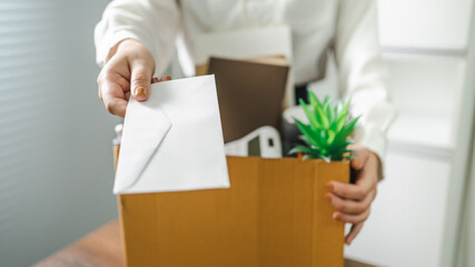 Business woman sending resignation letter and packing Stuff Resign Depress or carrying business cardboard box by desk in office. Change of job or fired from company - obrazy, fototapety, plakaty