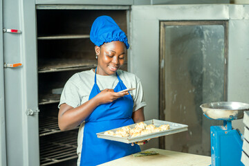 image of cheerful african woman in apron and head wrap, carrying tray with cookie- black baker...