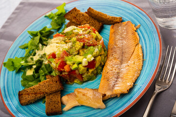 Image of delicious salad guacamole with fresh tomatoes and arugula served with grilled trout fillet at plate