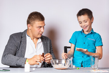 Chemistry education and training concept. Close-up of a boy and his dad doing a home chemical experiment, making slime from glue, sodium tetraborate and dyes