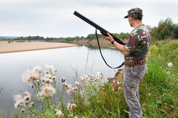 a hunter with a weapon stands on the river side