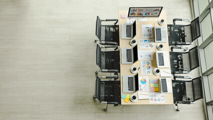Conference meeting room working table in company office full of laptop notebook computers black hot coffee cups and report data paperwork documents and black chairs with copy space on wooden floor