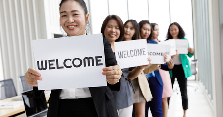Group of Asian female businesspeople joins together greeting and hold welcome words for a sign of...