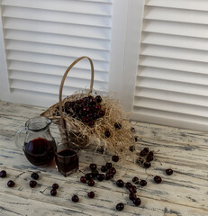 Cherry and cherry juice or wine on a wooden table, a decanter and a glass with juice, a basket with...