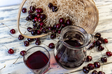 Cherry and cherry juice or wine on a wooden table, a decanter and a glass with juice, a basket with...