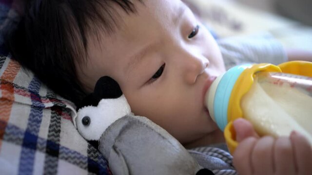 Chinese baby boy drink milk by holding bottle sleep beside penguin plush toy