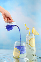 Woman's hand is pouring water from butterfly pea flower into a glass of lemon and honey tea. Butterfly pea or blue pea, Asia herb drink with lemon and honey. 