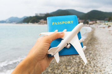Passport and toy plane in hand on the background of the sea, travel concept