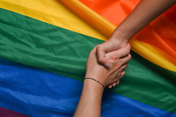 Two young women lesbian couple holding hands over LGBT pride flag.