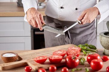 Crop cook sharpening knife in kitchen
