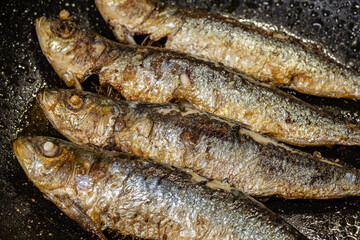 Sardines frying in a pan with oil.