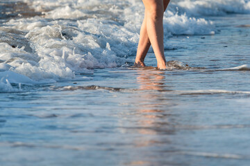 Beautiful legs of a young woman walking on a beach with waves rolling behind her feet
