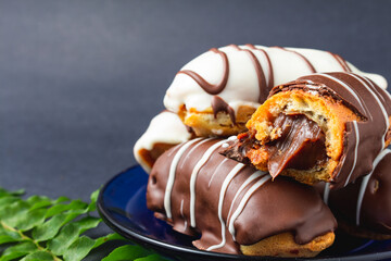 Chocolate bomb. Traditional Brazilian eclair bitten with apparent filling on a black background and branch of leaves. 