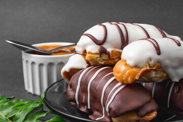 Bomb with dulce de leche filling. Traditional Brazilian éclair and container with dulce de leche on the side on a black background and branch of leaves. 