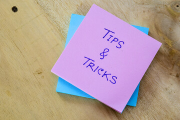 Tips and tricks handwritten text on sticky note pile placed on wooden desk. Top view. 