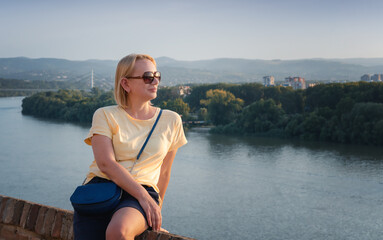 Beautiful adult blonde woman in sunglasses enjoying the view of the river at sunset