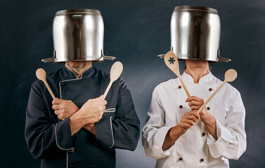 Two male chefs spoofing around with large pots - obrazy, fototapety, plakaty