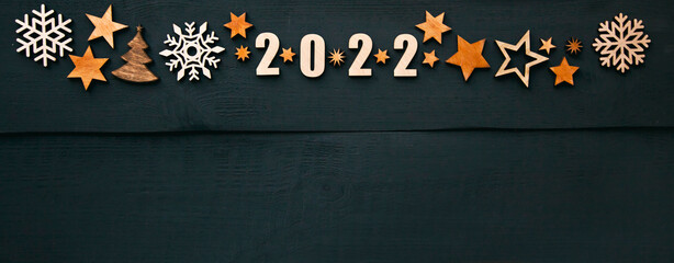 The beautiful christmas background with a lot of small wooden decorations and wooden numbers 2022 on the dark wooden desk.