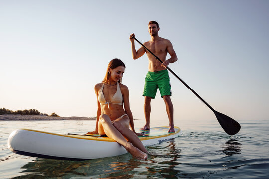 Couple of tourists young man and woman having fun paddleboarding at sea