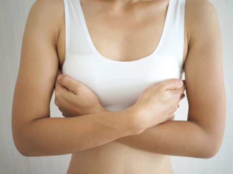 Young woman examining her breast for lumps or signs of breast cancer on white background. closeup photo, blurred.