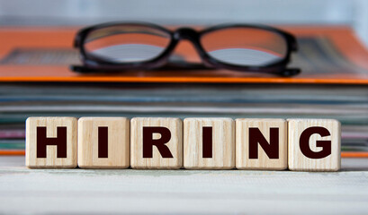 Obraz premium HIRING - word on wooden cubes on the background of a folder with documents and glasses