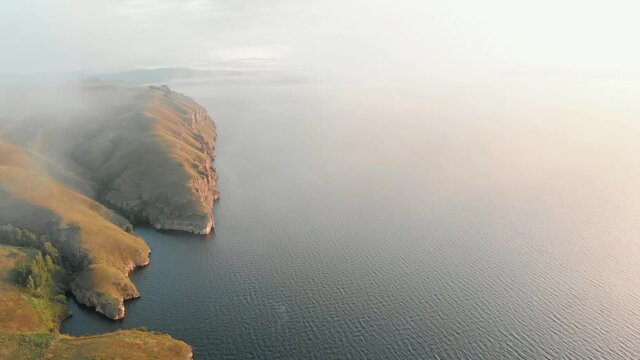 Flight near the coast with rocky cliffs. dawn of the sun, fog and clouds, waves on the water Krasnoyarsk Sea Saragash