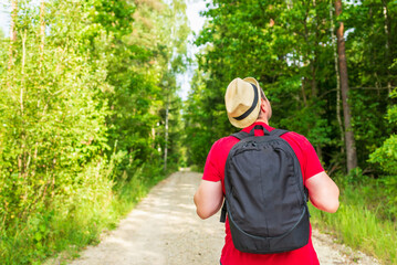 Naklejka premium Back view of young man with backpack traveling alone forest on warm summer day.Tourism and active lifestyle concept.