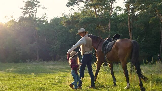 A cowboy with a horse and his beautiful daughter are walking in the pasture