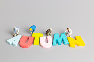 Miniature people worker team painting of Autumn with place for text on grey background  , Hello Autumn concept