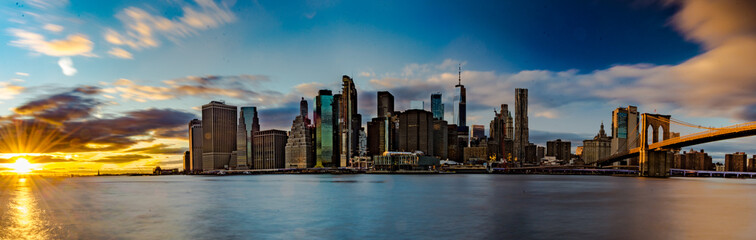 Fototapeta na wymiar Lo straordinario skyline di New York City. Fiume con palazzi illuminati come sfondo. Foto Panoramica in lunga esposizione al tramonto