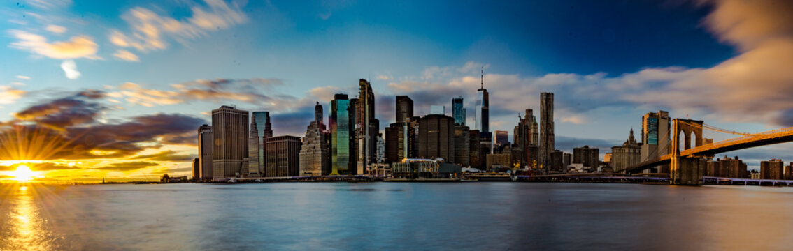 Lo straordinario skyline di New York City. Fiume con palazzi illuminati come sfondo. Foto Panoramica in lunga esposizione al tramonto