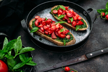 Bruschetta with pesto and tomatoes on a dark background