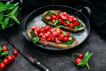 Bruschetta with pesto and tomatoes on a dark background