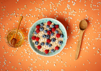 Healthy breakfast - oatmeal with honey, blueberries and raspberries on orange background. Flat lay