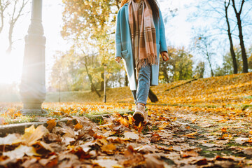Legs of unrecognosable woman wearing brown boots and jeans in autumn yellow foliage walking in park...