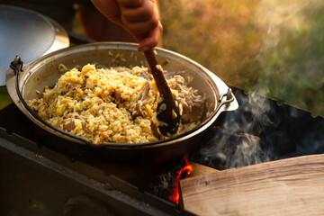 The female hand of the cook is stirring the pilaf with a spoon.