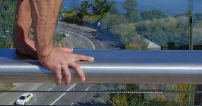 Close up hands  of professional acrobat performing dangerous trick on the railing of the glass bridge against backdrop of city. Caucasian guy walking on hands  on a narrow metal pipe
