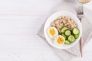Breakfast oatmeal porridge with boiled egg, cucumber and sesame seed. Healthy balanced food. Top view, flat lay