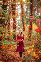 girl in a red dress in the autumn forest. A beautiful fairy-tale forest. A bouquet of leaves in...