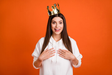Portrait of attractive amazed cheerful girl wearing crown choose me isolated over bright orange...