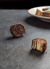 Traditional oriental sweetness Rahat locum with chocolate and cocoa on a gray background. Plate with multi-colored Turkish delight. Bitten off dessert. Side view. Copy space.