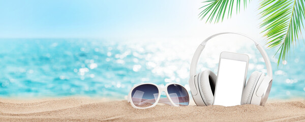 Smartphone, sunglasses and headphones on tropical sea beach