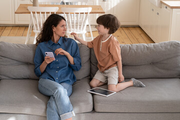 Tired mother try to read messages or surf internet on smartphone after work sitting on couch with...