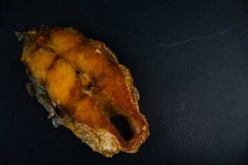Pieces of fried fish are placed on a black plate.