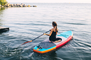 Close-up of a girl floating on a sup board. The concept of water sports, relaxation and self-immersion. Lonely woman alone on a board against a background of water and a pier.