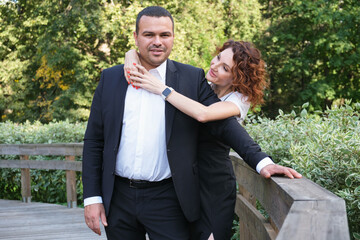 Portrait of a couple in love. A Middle Eastern man in a business suit with his curly-haired wife in a black dress. Woman hugs a man and looks at him with a loving look. Happy husband and wife.