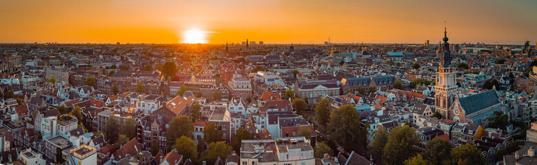 Beautiful evening panorama of Amstedam city looking towards the west with beautiful sunset and sun setting down over Amsterdam. Drone view. - obrazy, fototapety, plakaty