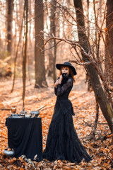 witch in the autumn forest. A woman with a black cat is preparing for Halloween